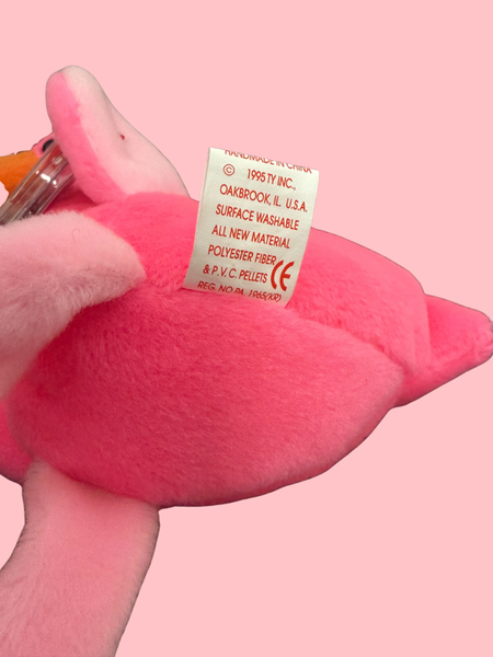 Pink plush toy with a label on a pink background