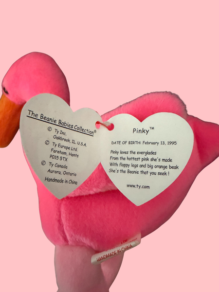 Pink flamingo plush toy with a heart-shaped tag on a pink background